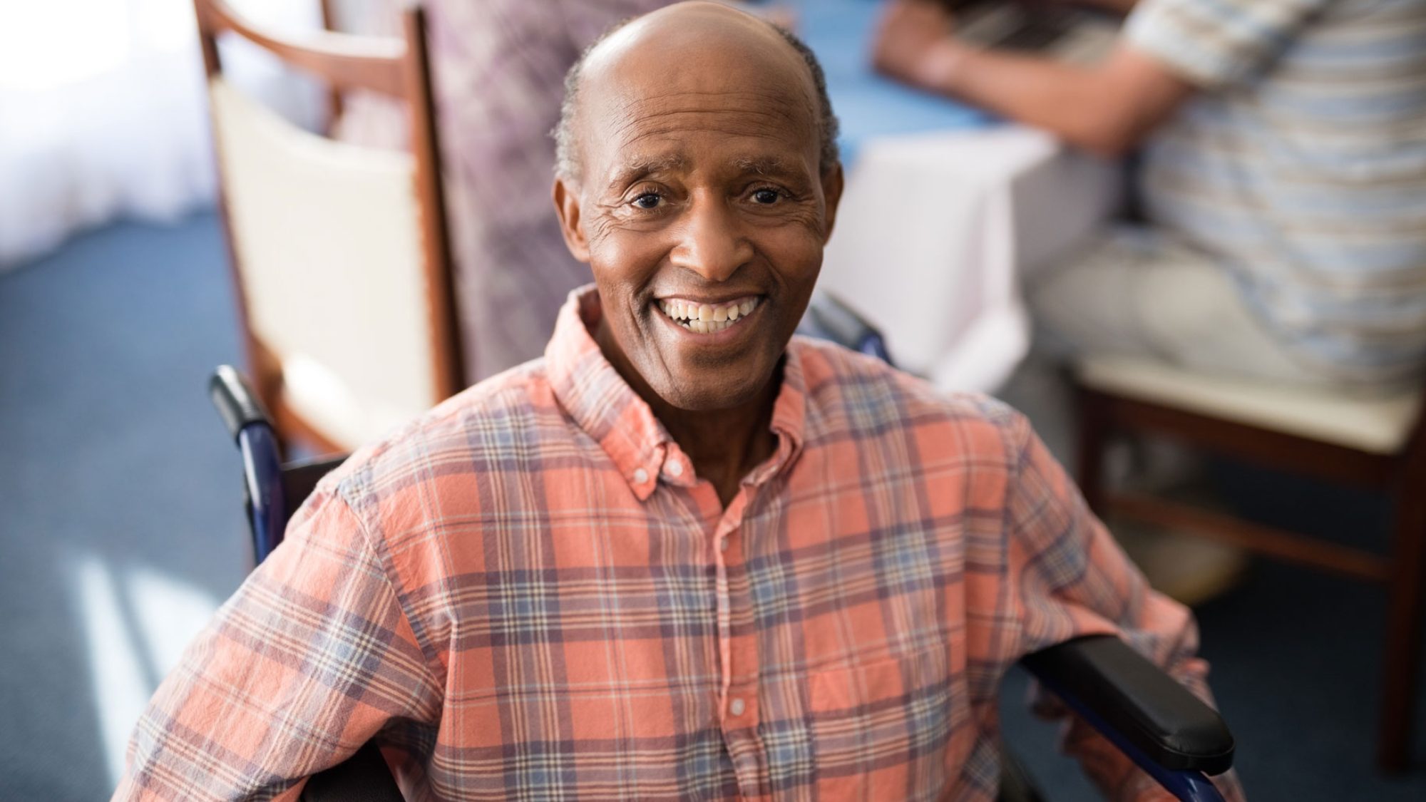 An elderly black man smiling at the camera and sitting in a wheelchair