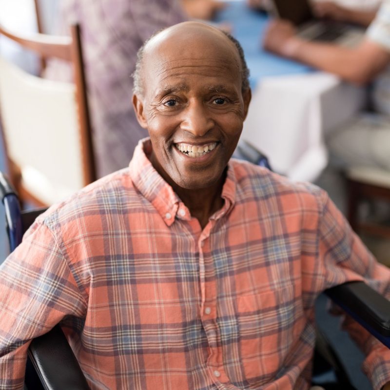An elderly black man smiling at the camera and sitting in a wheelchair