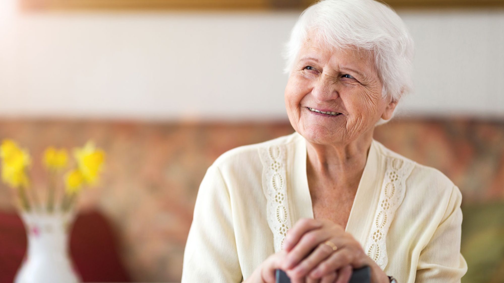 An older woman with white hair leaning on a cane and smiling, looking to the left