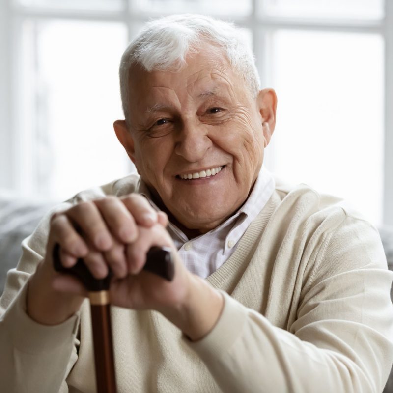 An elderly man smiling and leaning on his cane