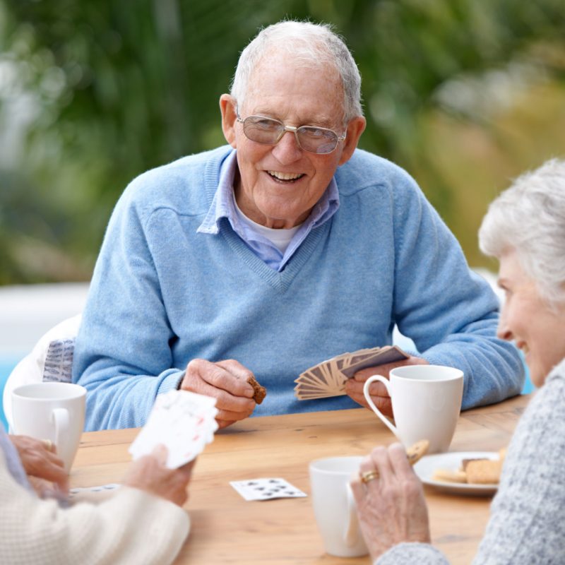 An older man playing cards with two older women.