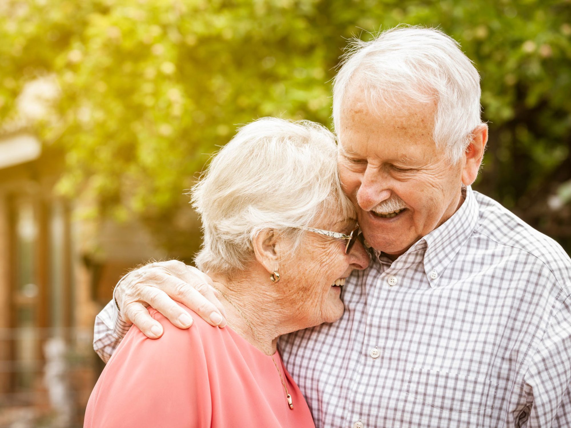 An older man and woman happily hugging outside