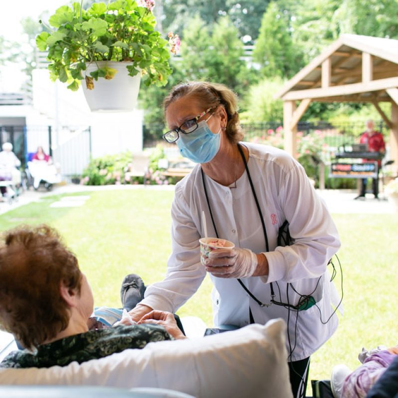 A nurse helping a resident enjoy an ice cream while watching a concert.